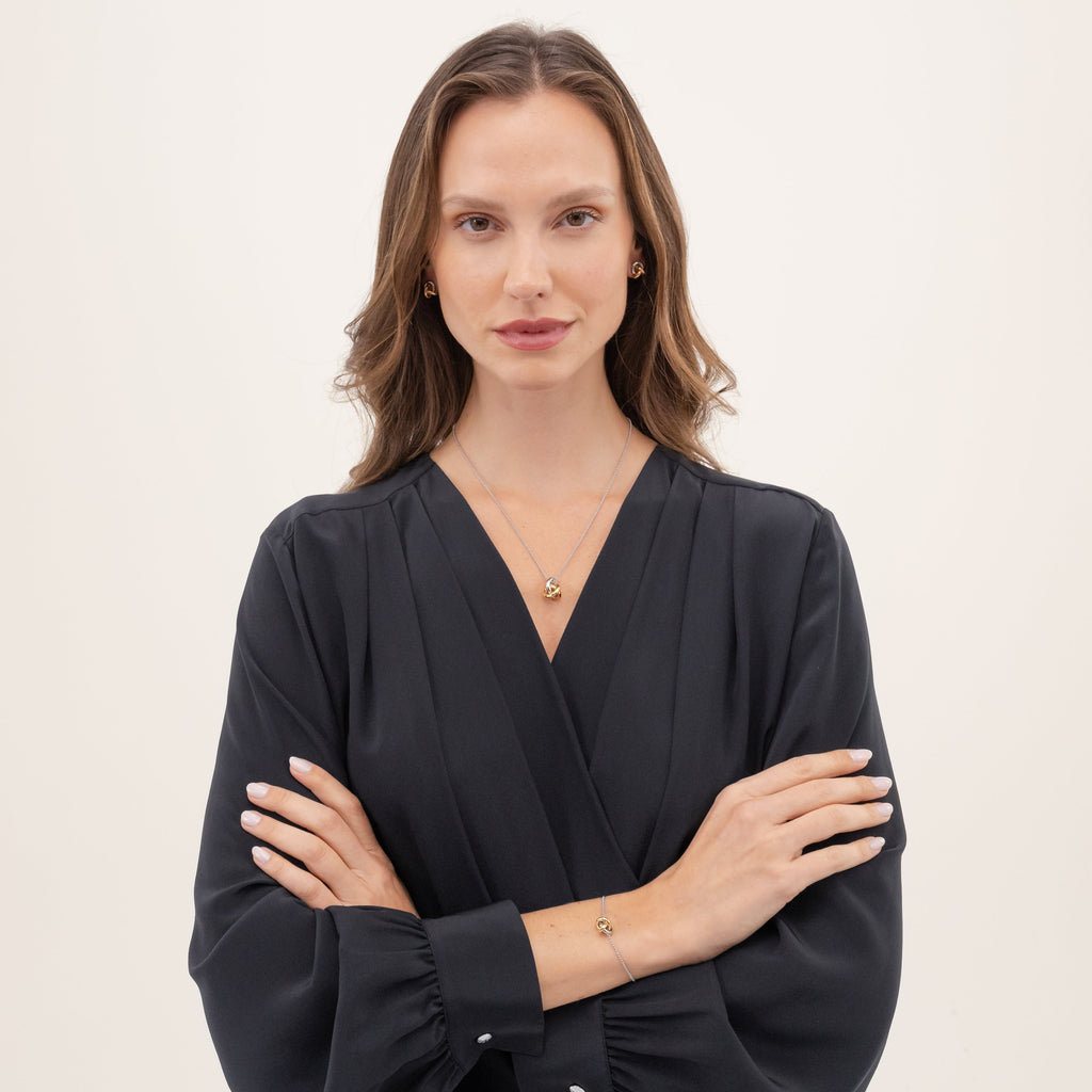 Woman in navy wrap dress with jewelry, arms crossed, beige background.
