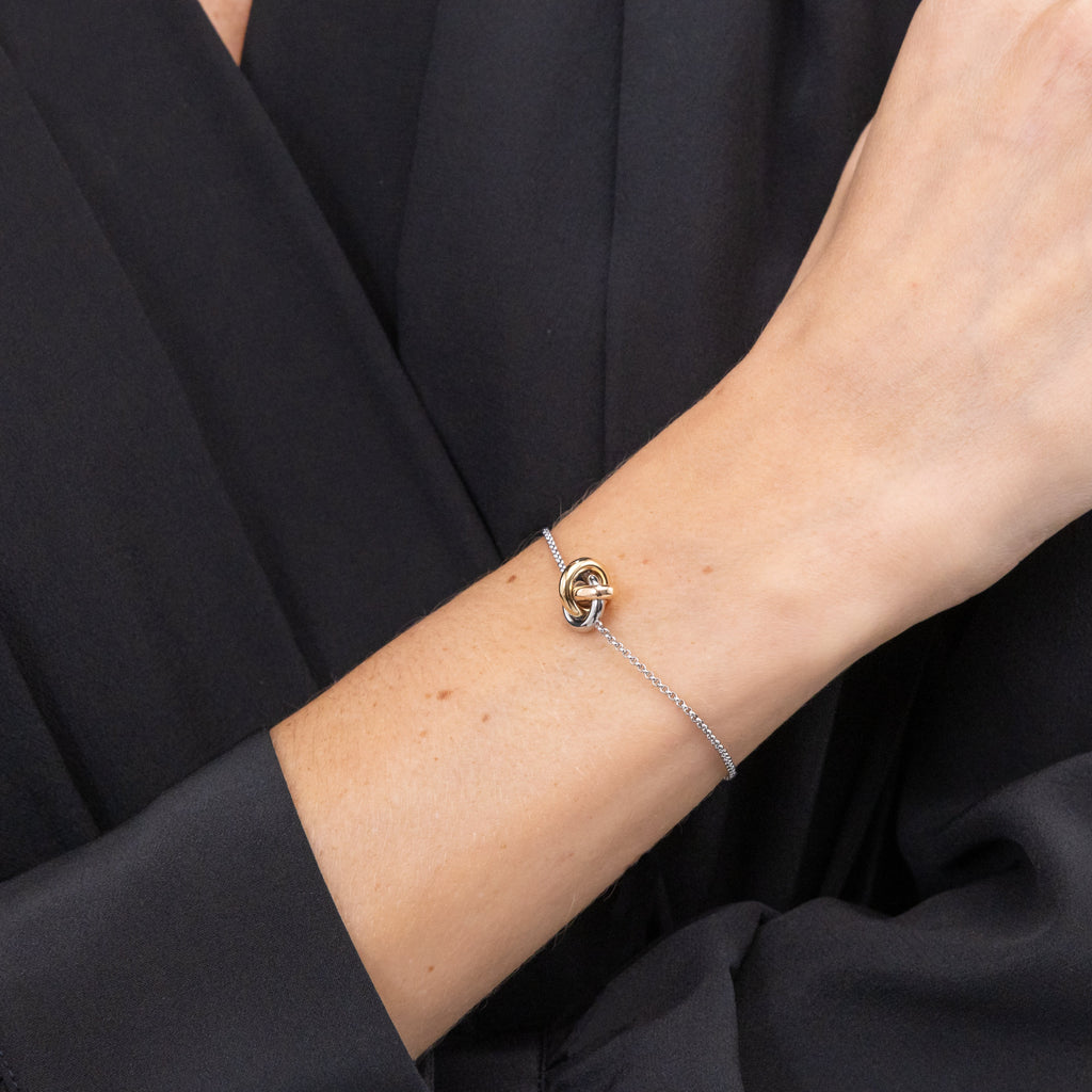 Close-up of a bracelet on a woman's arm against a black fabric background.