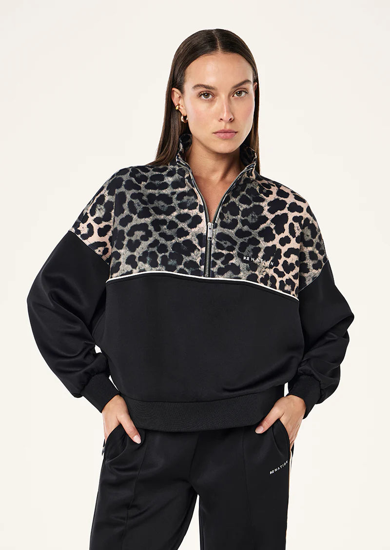Woman wearing a black and leopard print half-zip sweatshirt on a white background