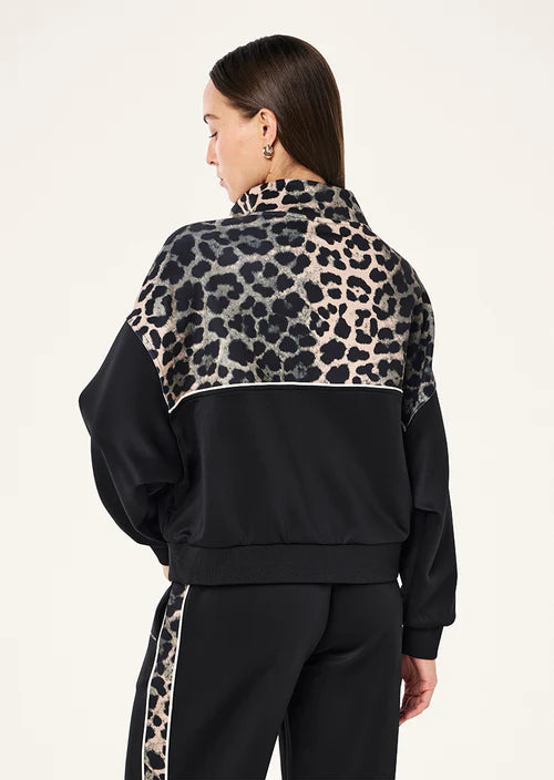 Person wearing a black tracksuit with leopard print details on a plain background