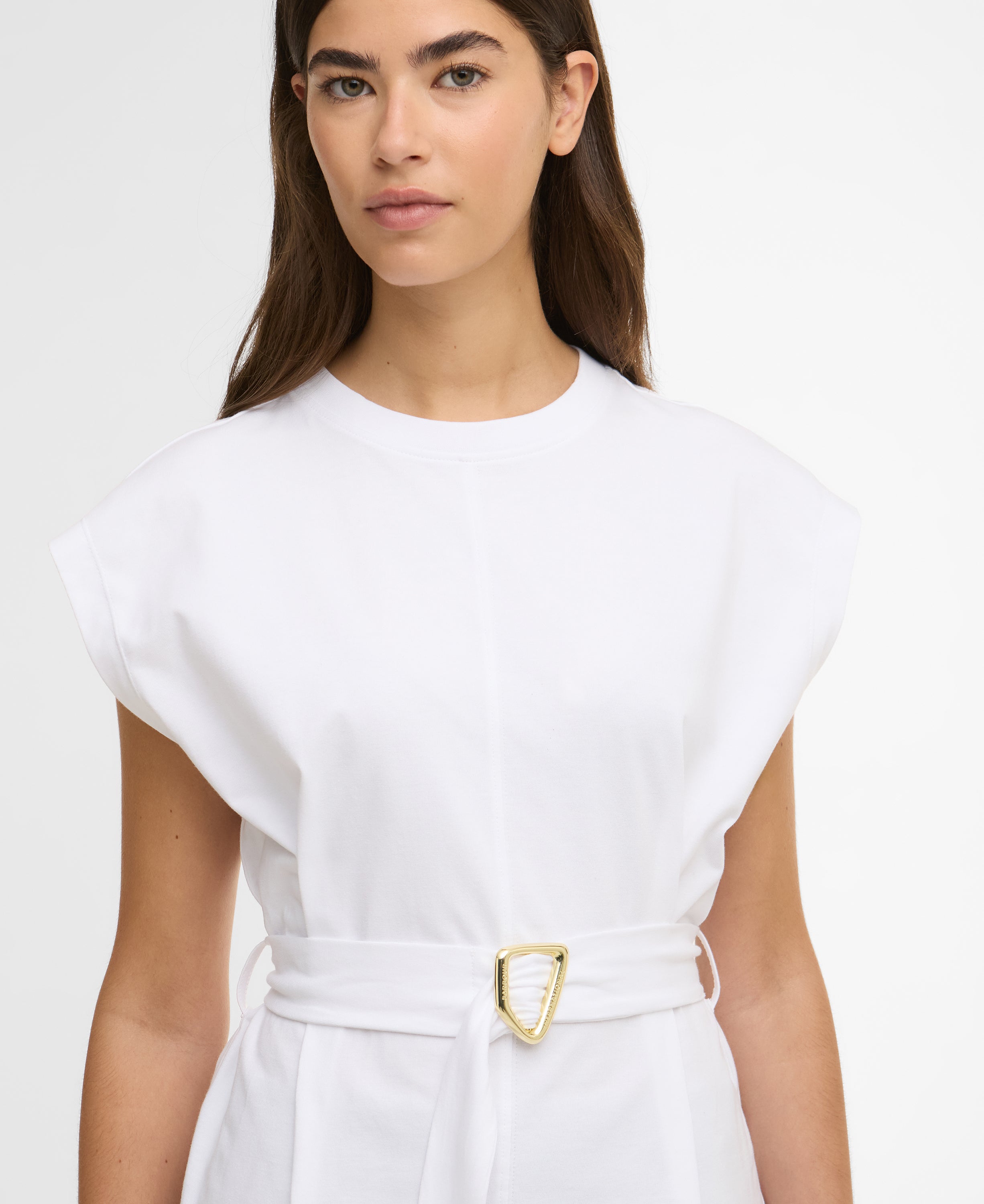 Woman wearing a white dress with a gold belt on a plain background