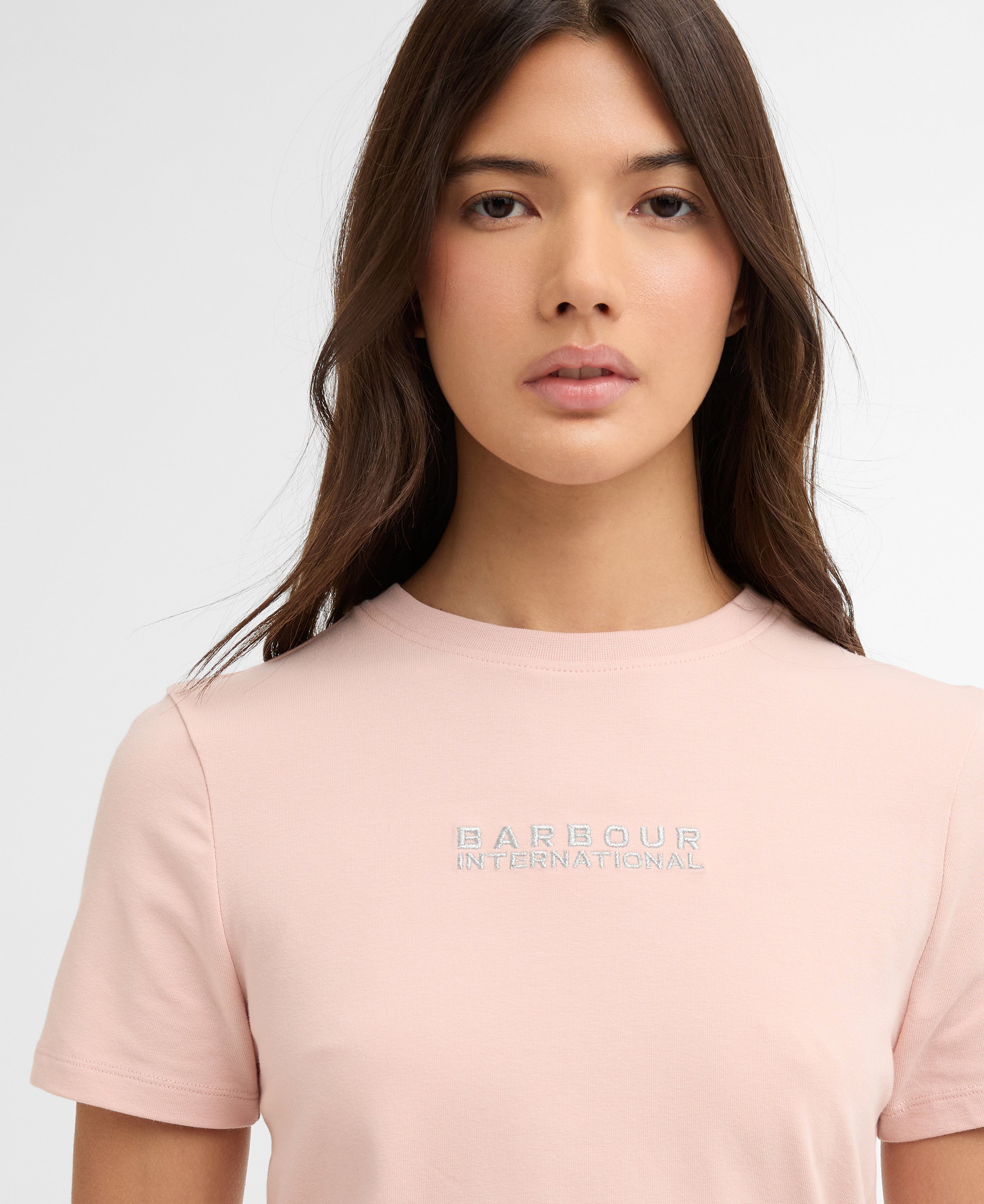 Woman wearing a light pink t-shirt with a brand logo on a white background