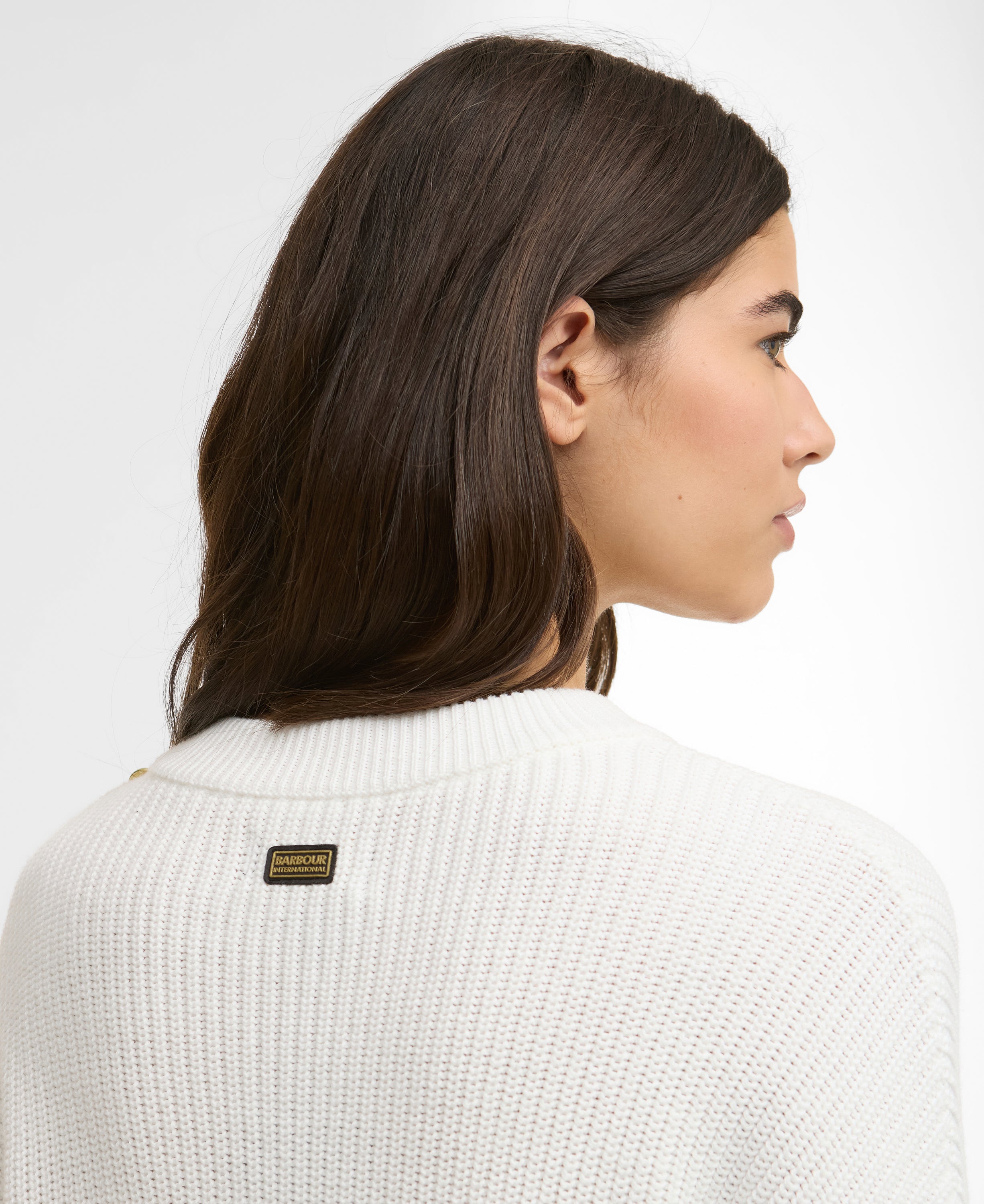Woman wearing a white sweater with a brand label on a light gray background