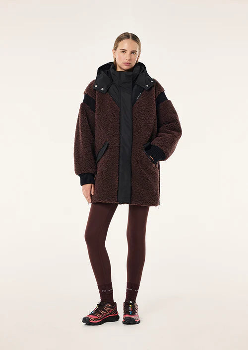 Person wearing a brown coat with black accents on a white background