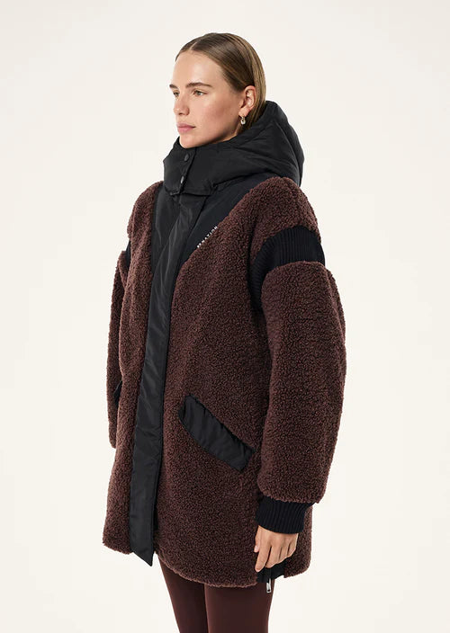 Woman wearing a brown teddy coat over a black jacket on a white background