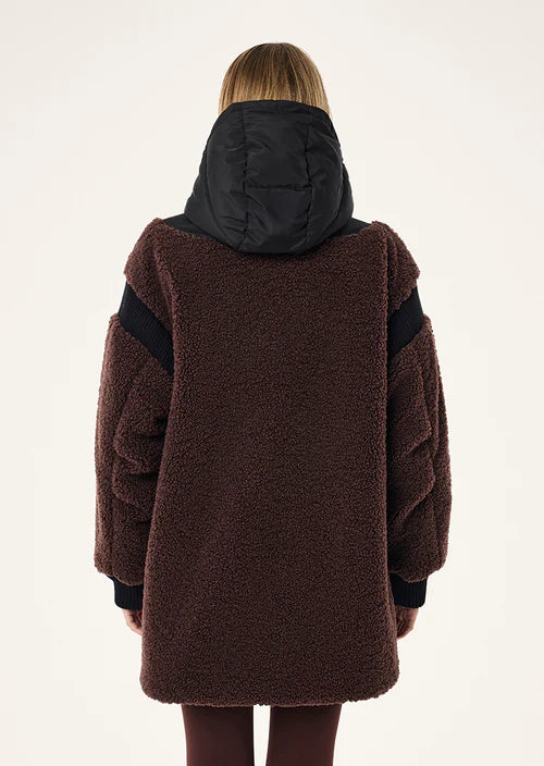 Person wearing a brown coat with black sleeves on a white background