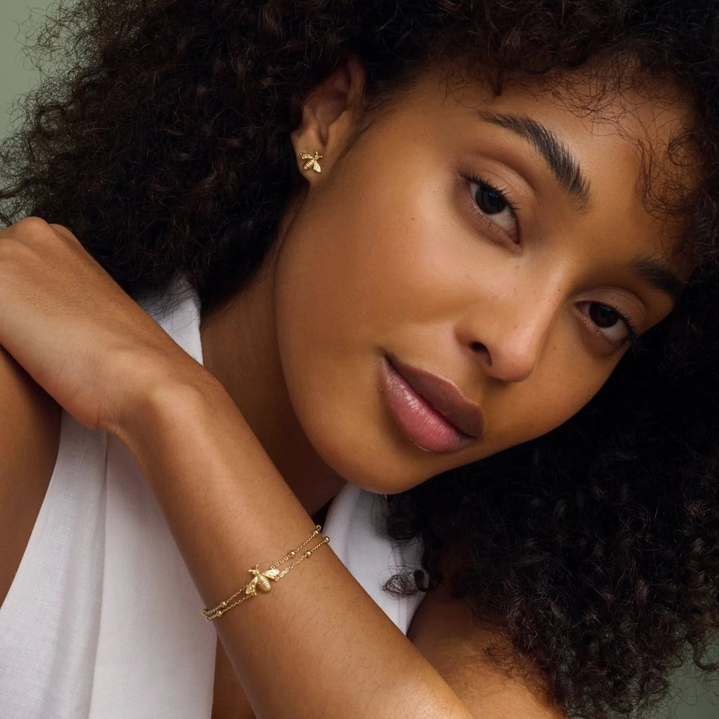 Model wearing gold bee earrings and a gold bee bracelet.