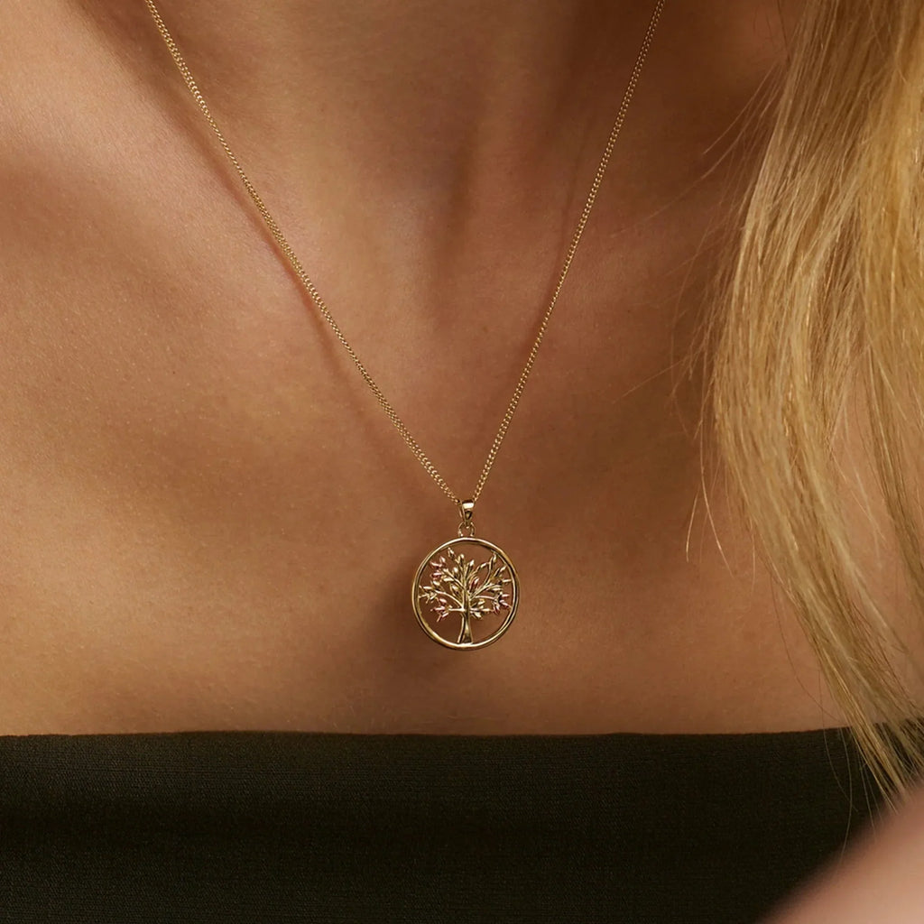 A woman wearing a gold tree of life pendant necklace.
