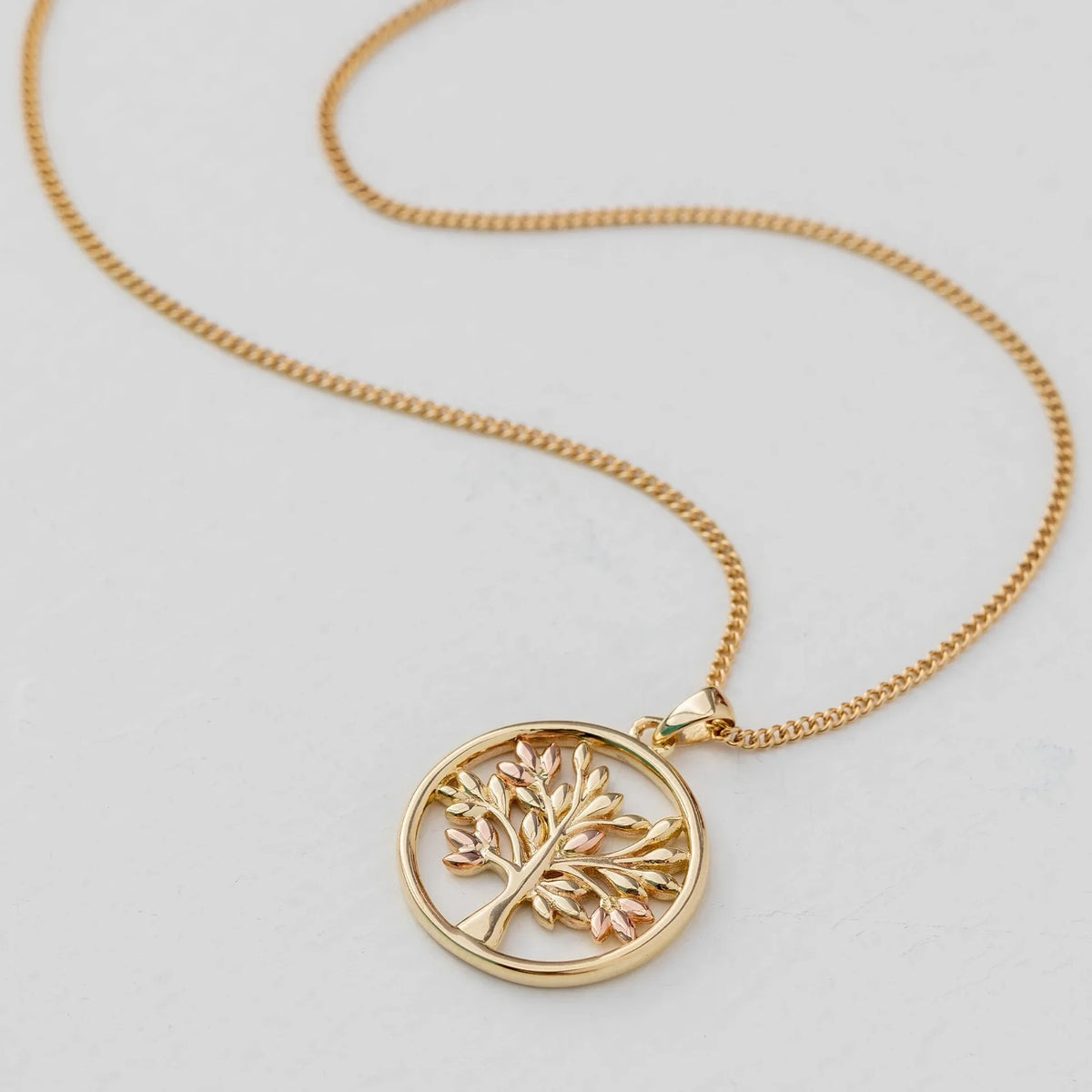 Gold necklace with tree pendant on white.