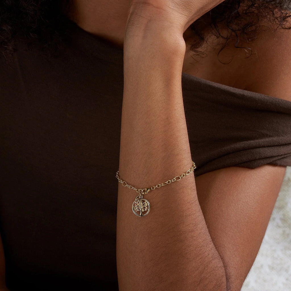 Gold bracelet with tree charm on person's arm.
