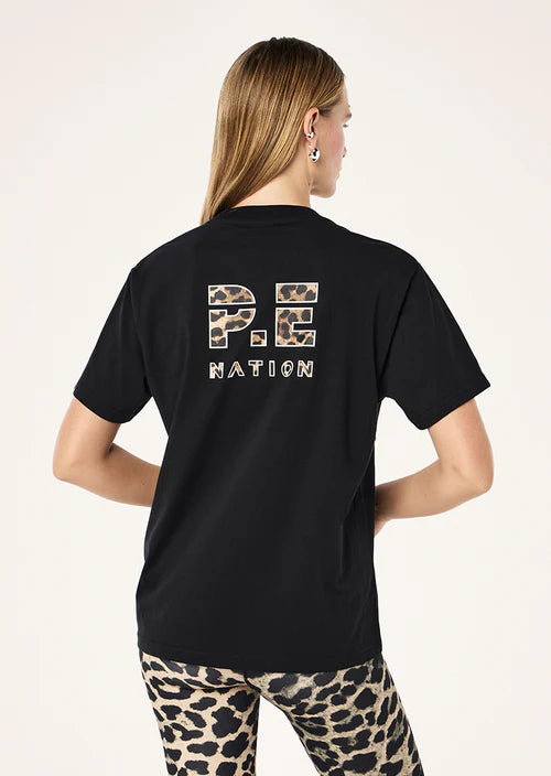 Person wearing a black t-shirt with 'P.E. Nation' text on the back, standing against a light pink background.