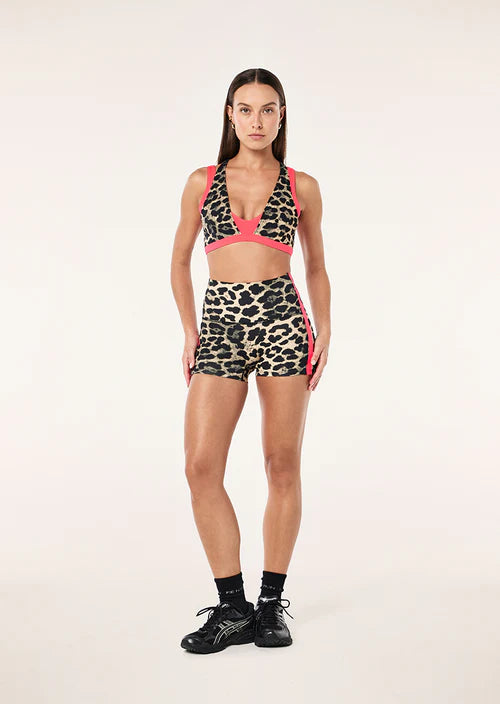 Woman wearing a leopard print sports bra and shorts set with pink accents on a white background