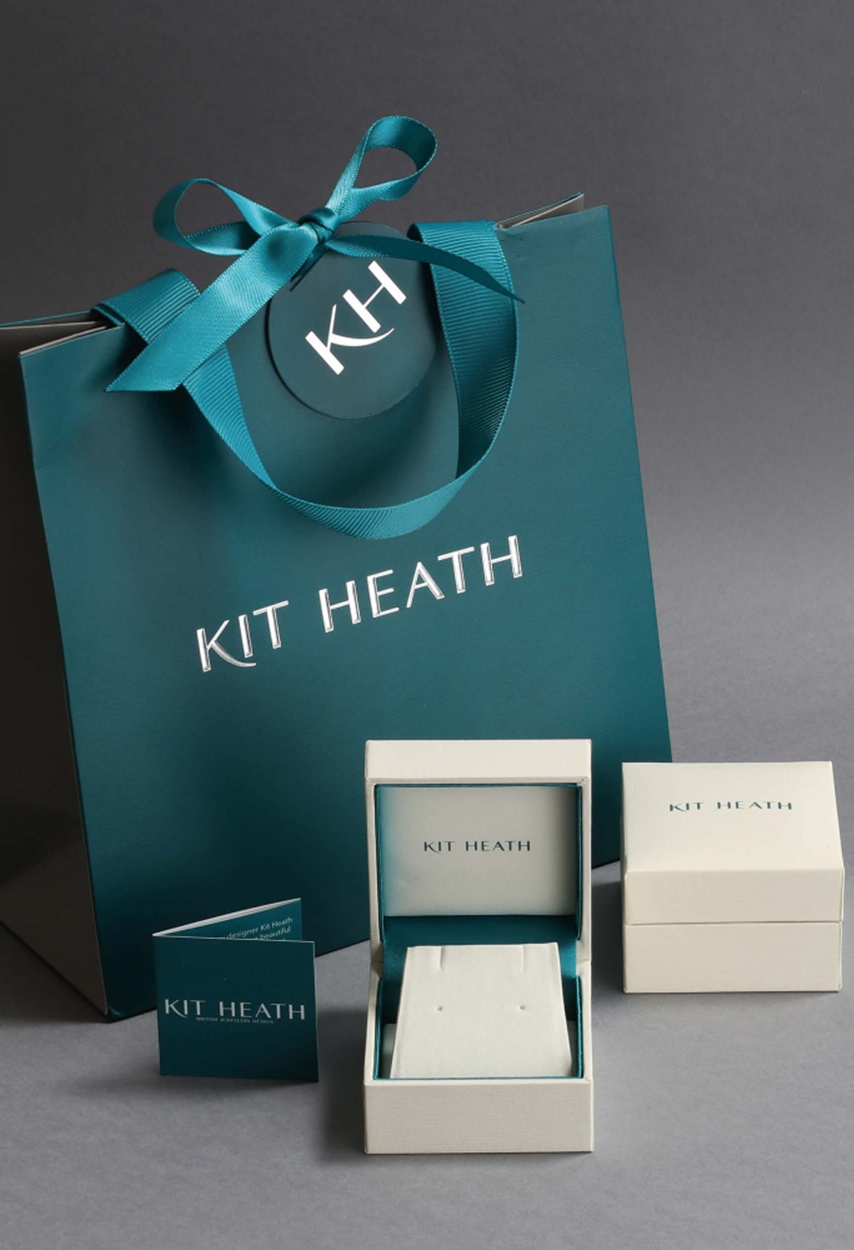 Kit Heath packaging showcasing the Glisten Pave CZ Stud Earrings. Jewelry box and gift bag with the brand logo.