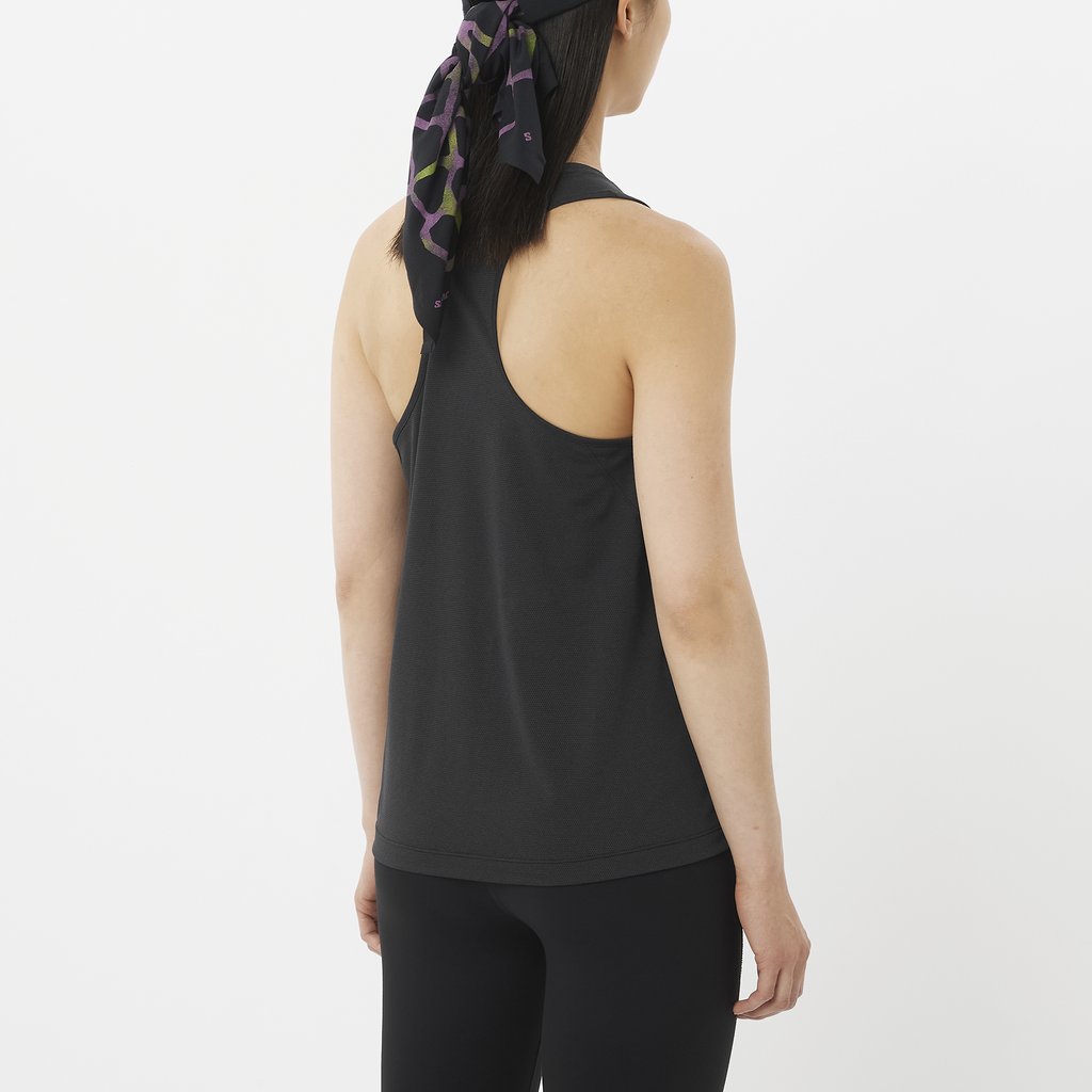 Person wearing a black tank top and leggings with a headscarf on a white background
