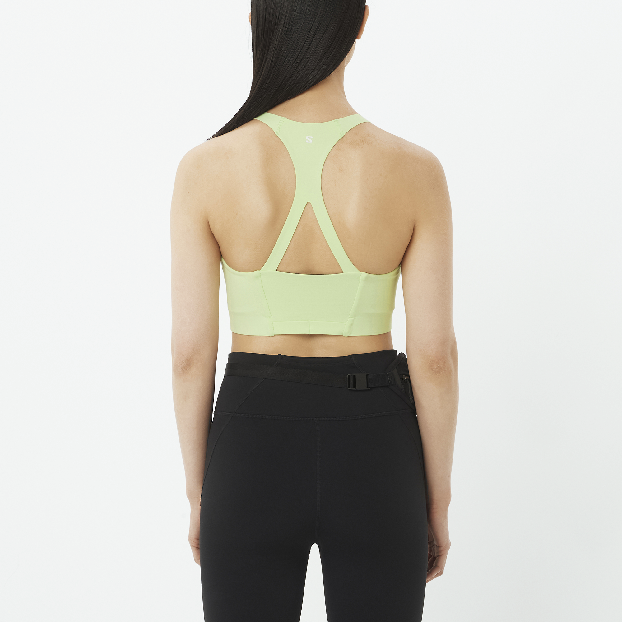 Person wearing a light green sports bra and black leggings on a white background