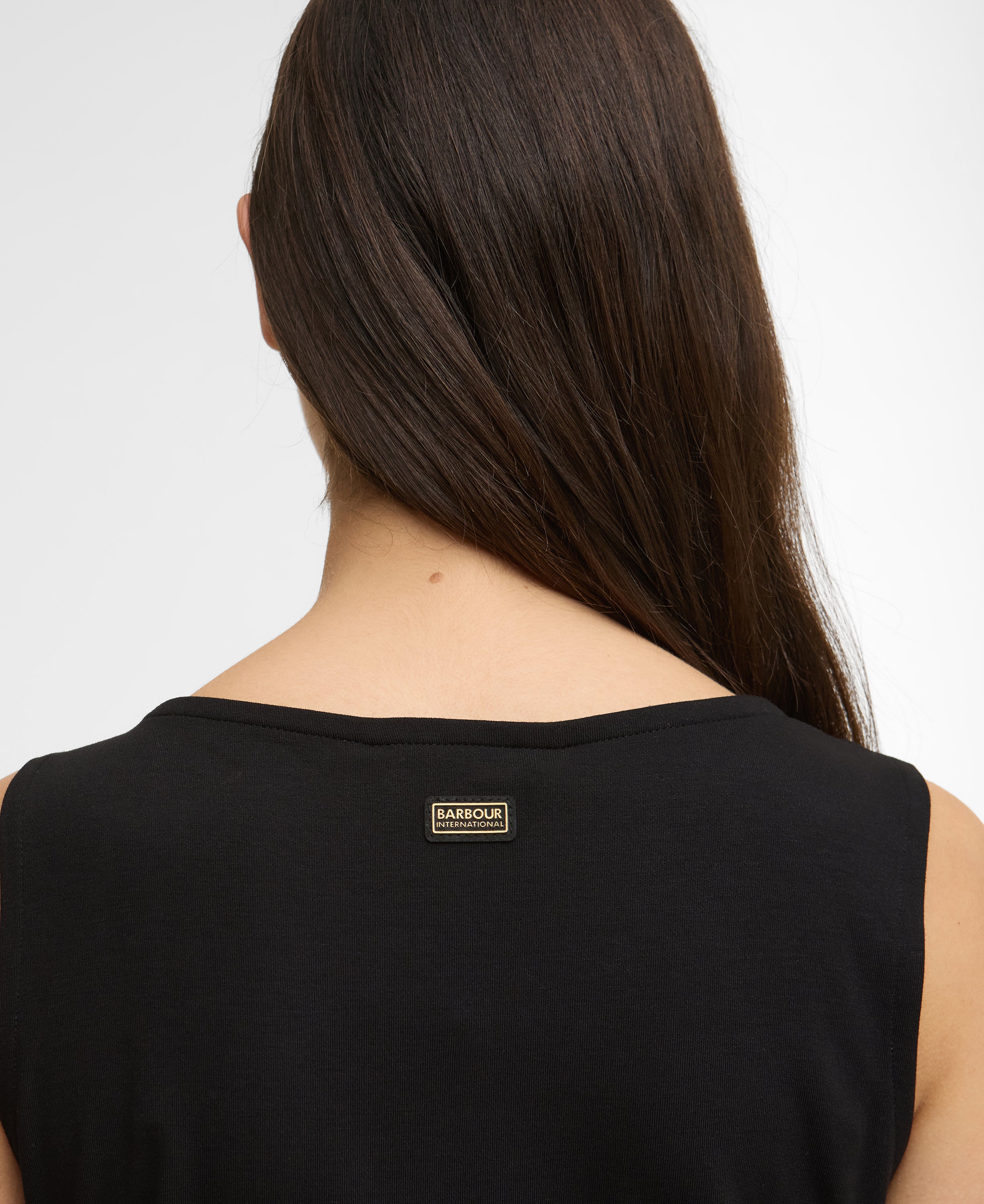Person wearing a black sleeveless top with a brand label on a white background