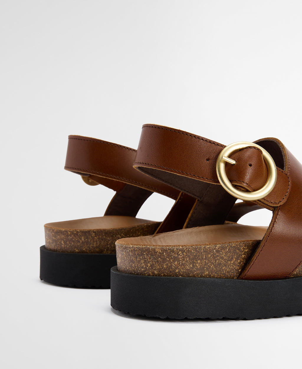 Brown sandals with a gold buckle on a light gray background