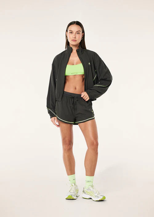 Woman wearing a grey jacket, green sports bra, and shorts on a white background