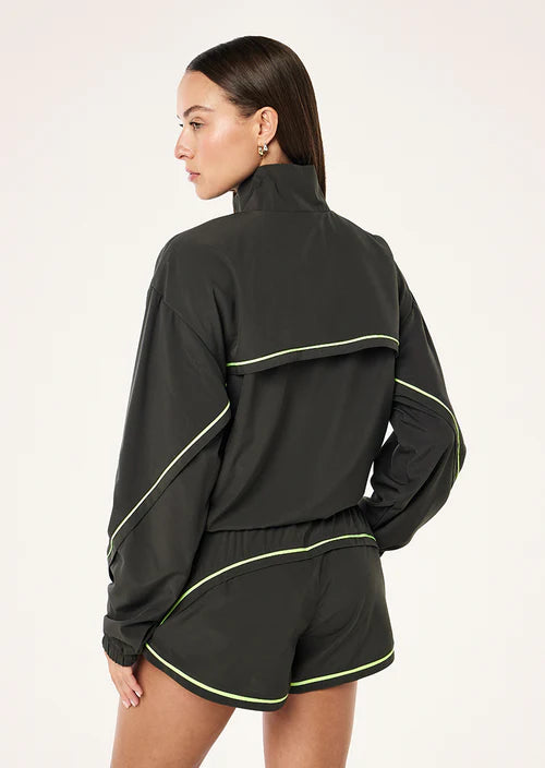 Woman wearing a grey tracksuit with lime green piping on a white background