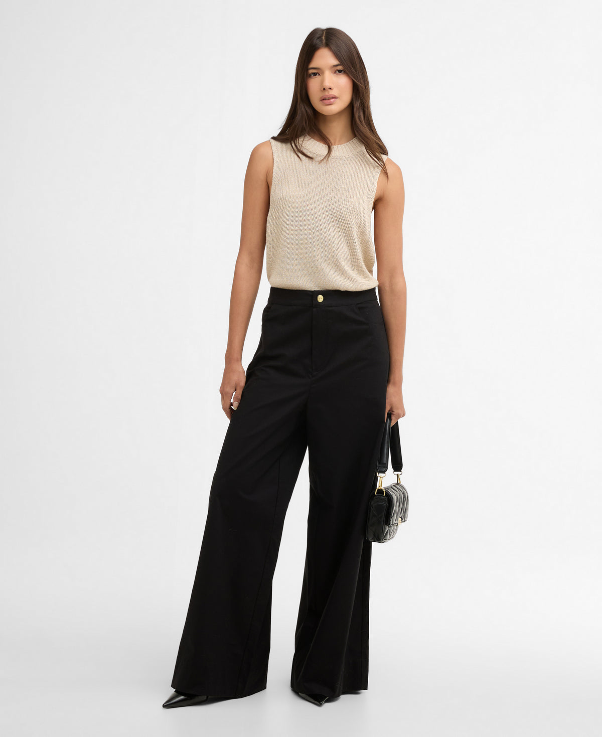 Woman wearing a beige sleeveless top and black high-waisted pants on a white background