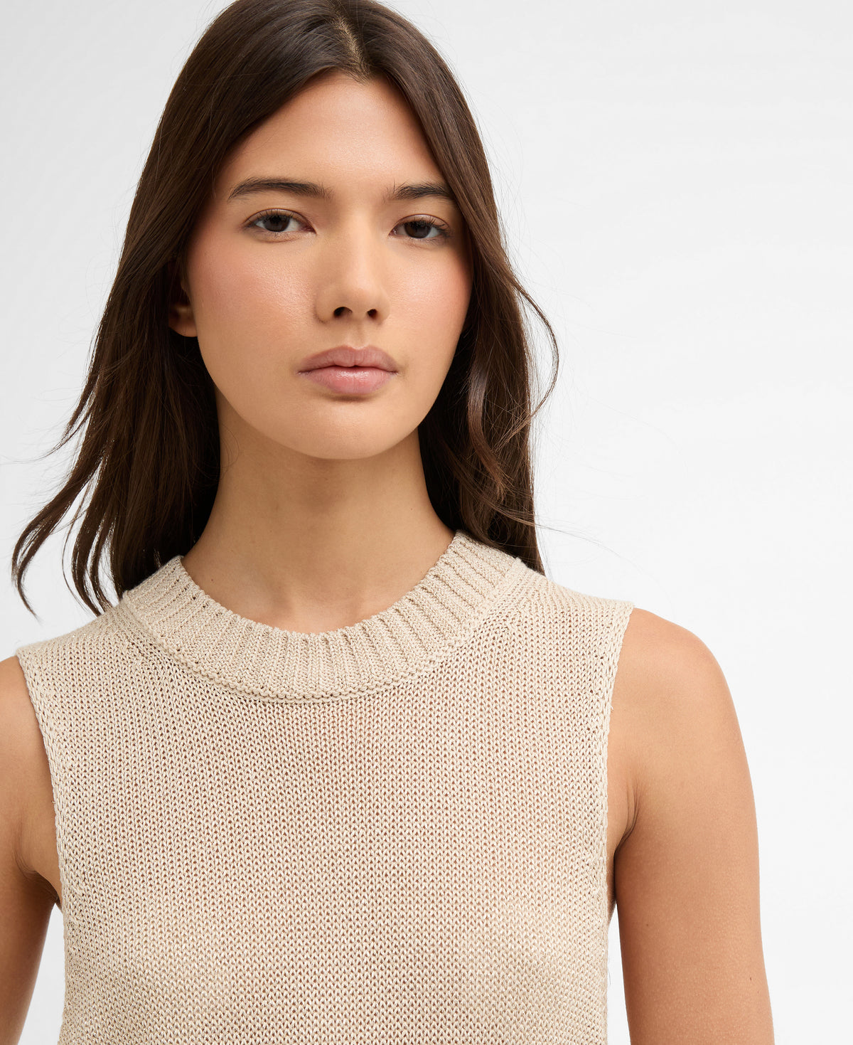 Woman wearing a beige sleeveless knitted top against a plain background