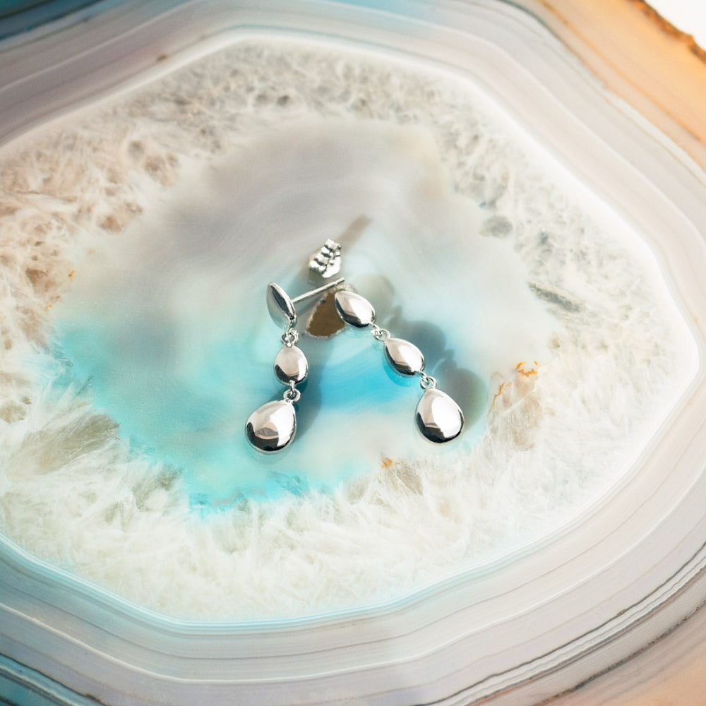 Close-up of silver drop earrings on an agate slab.