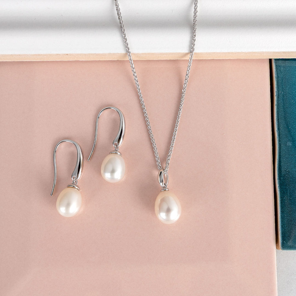 Pearl pendant necklace and pearl drop earrings on a pink and blue surface.
