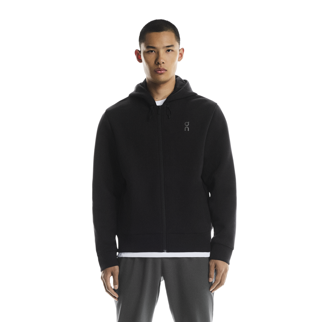 Person wearing a on running black zip hoodie with a chest on logo on a white background. wearing with on grey swetpants