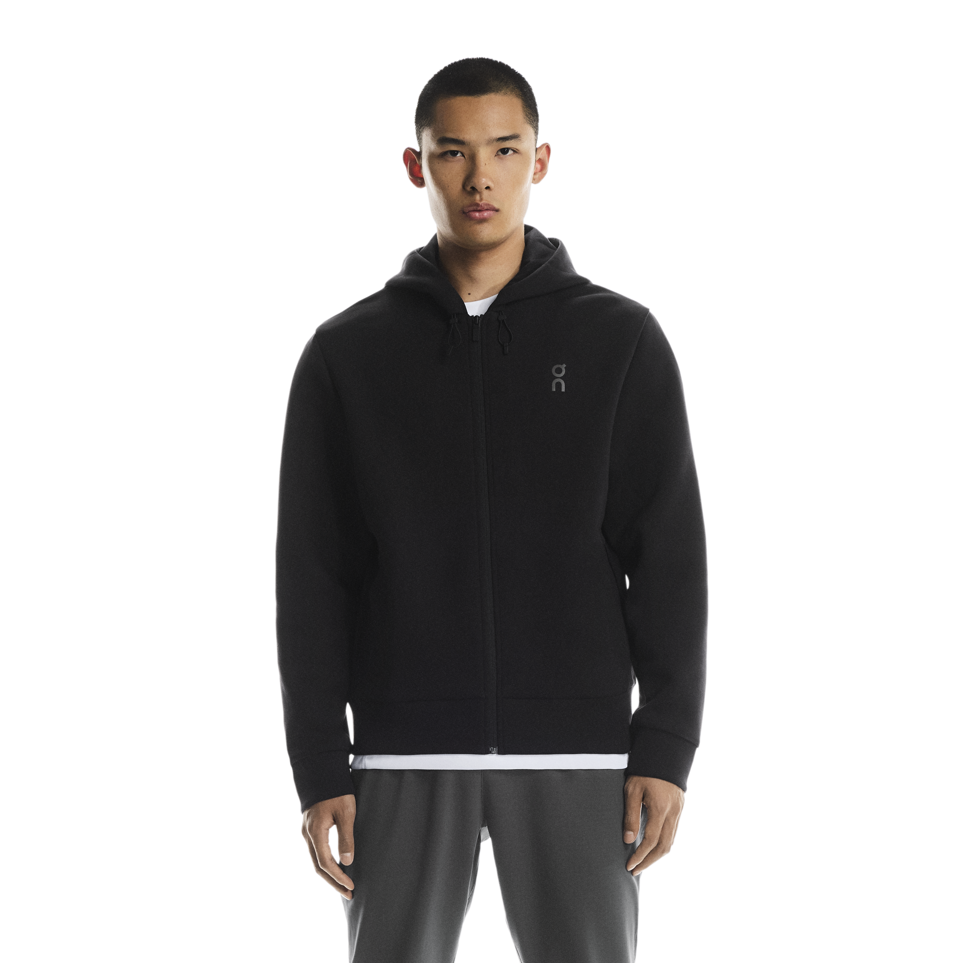 Person wearing a on running black zip hoodie with a chest on logo on a white background. wearing with on grey swetpants
