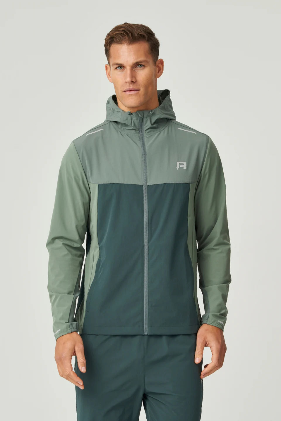 Man wearing a green windbreaker jacket with a reprimo brand logo on chest on a light grey background