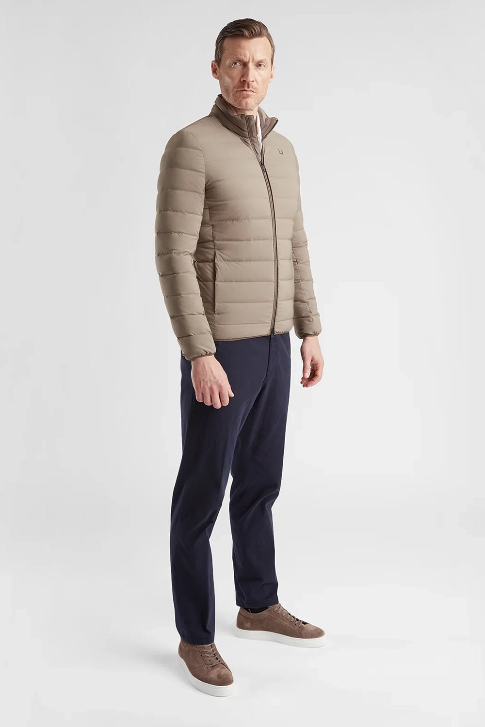 Man wearing a UBR beige quilted jacket, navy pants, and brown shoes on a white background
