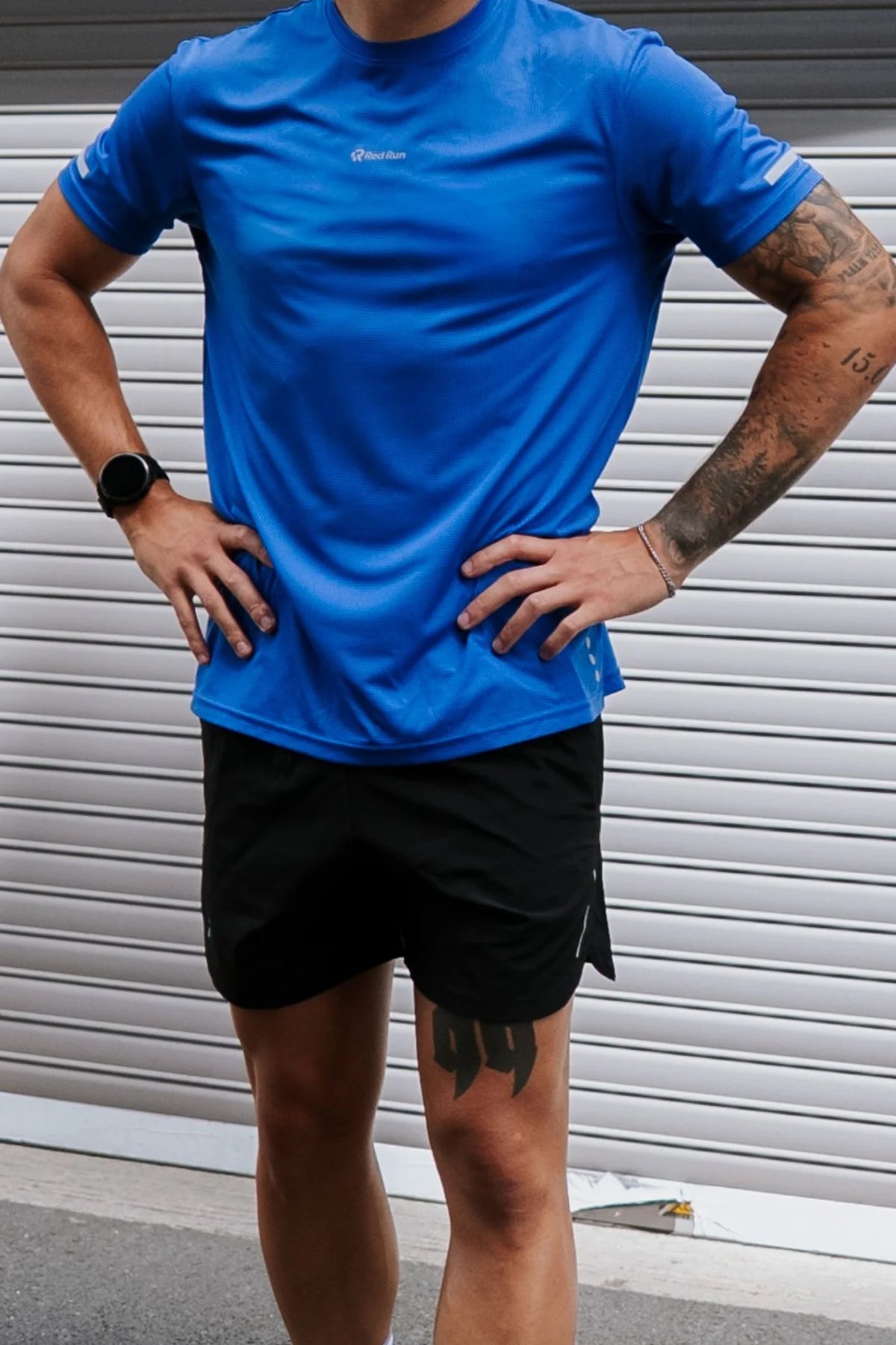 Person wearing a blue athletic shirt and black shorts standing against a metallic background