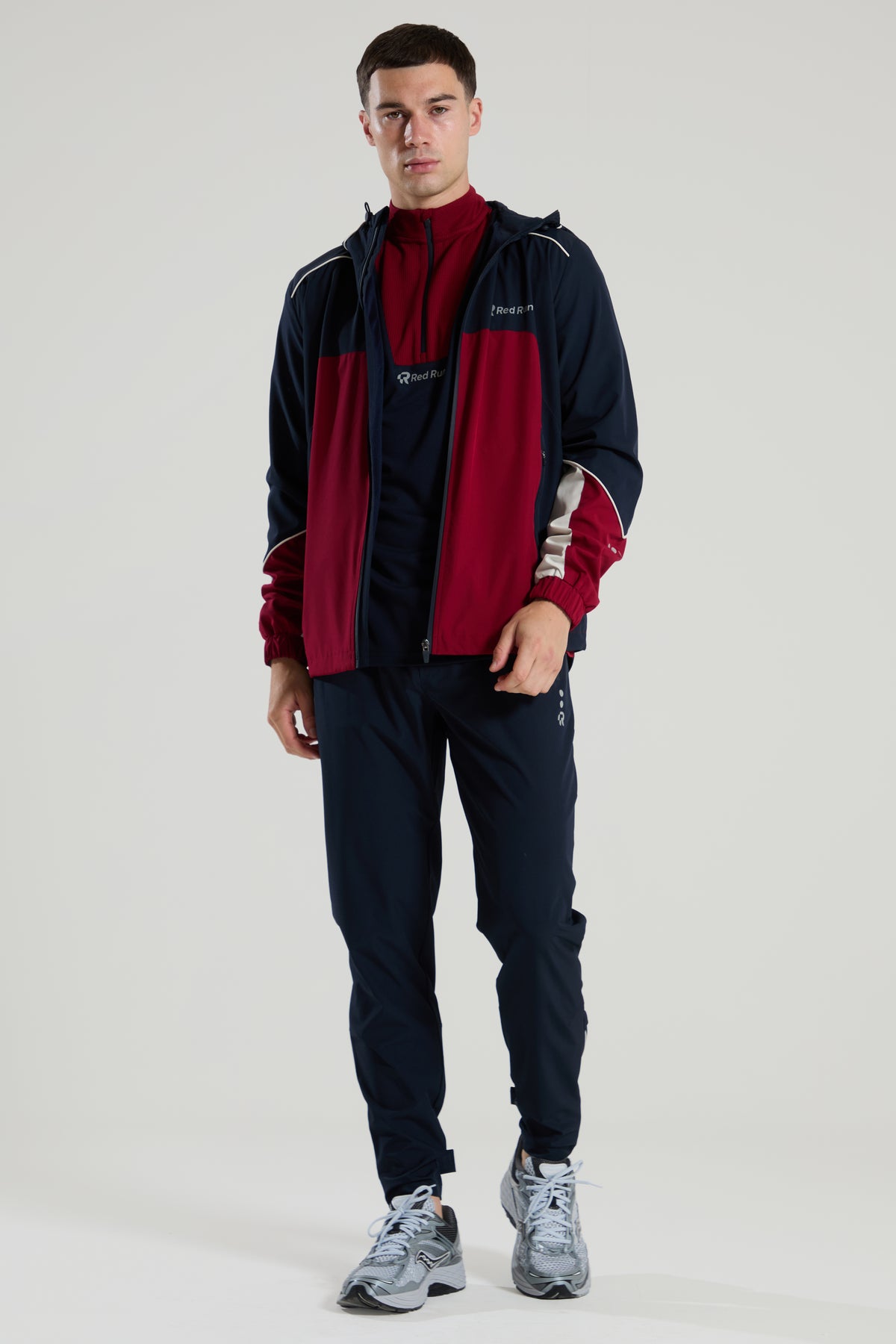 Man wearing a red run burgundey and navy tracksuit with a logo on a white background