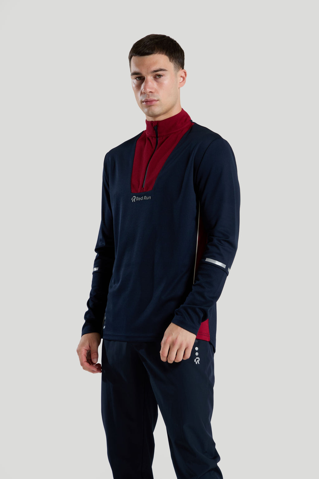 Man wearing a navy t1/4 zip tracksuit top with red accents on a light gray background