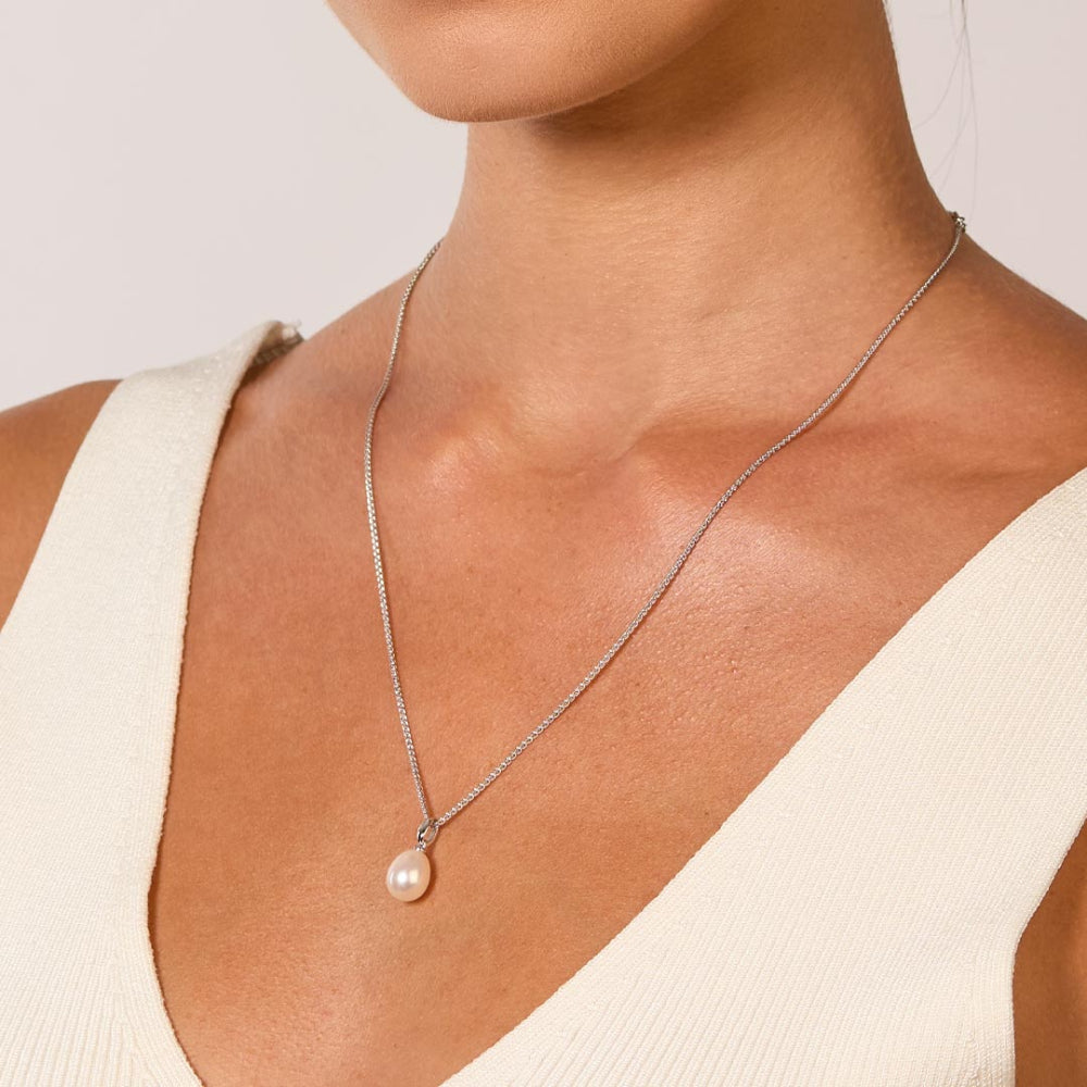 A woman wears a silver chain necklace with a single pearl pendant.