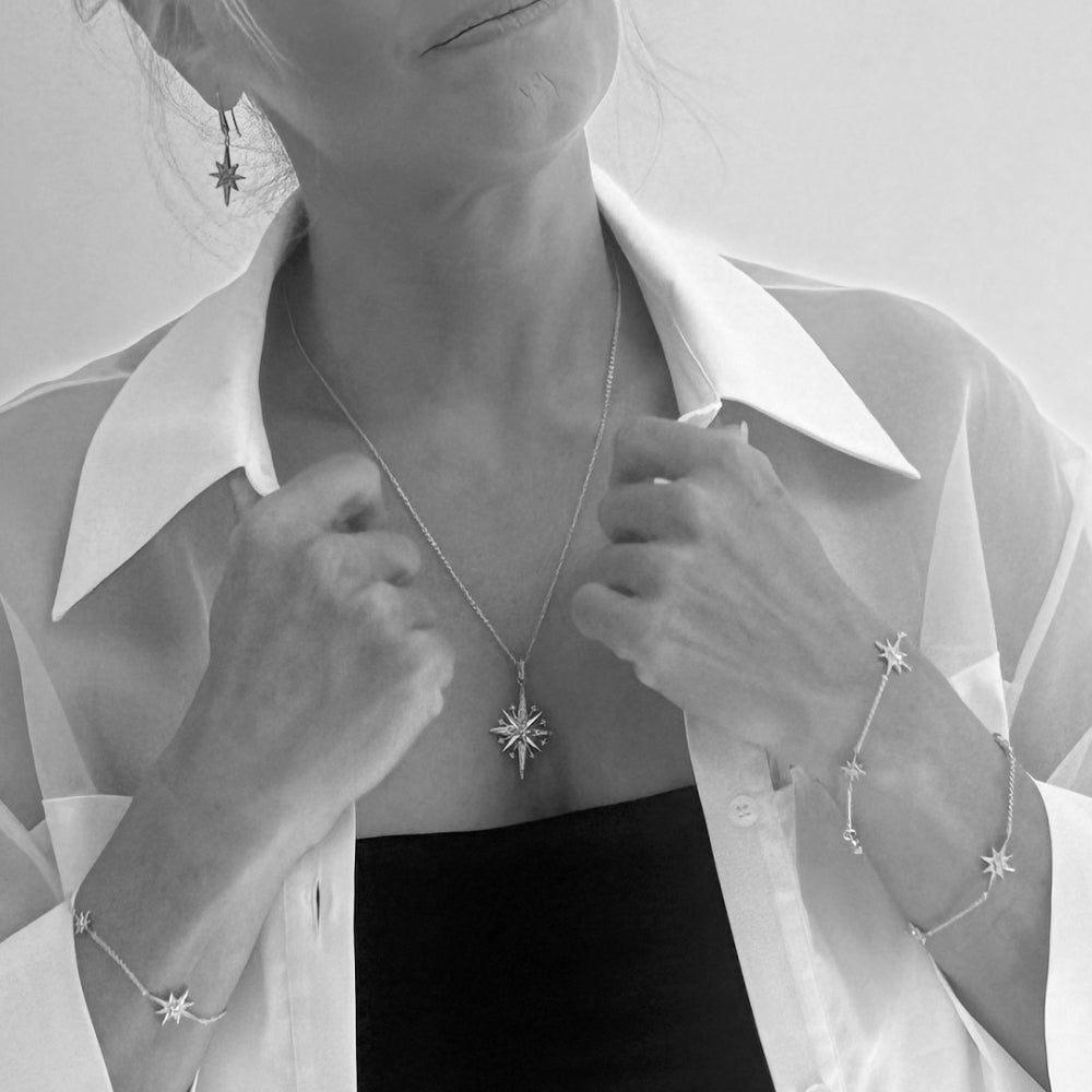 Black and white studio shot of a woman wearing star jewelry and a white blouse. 
