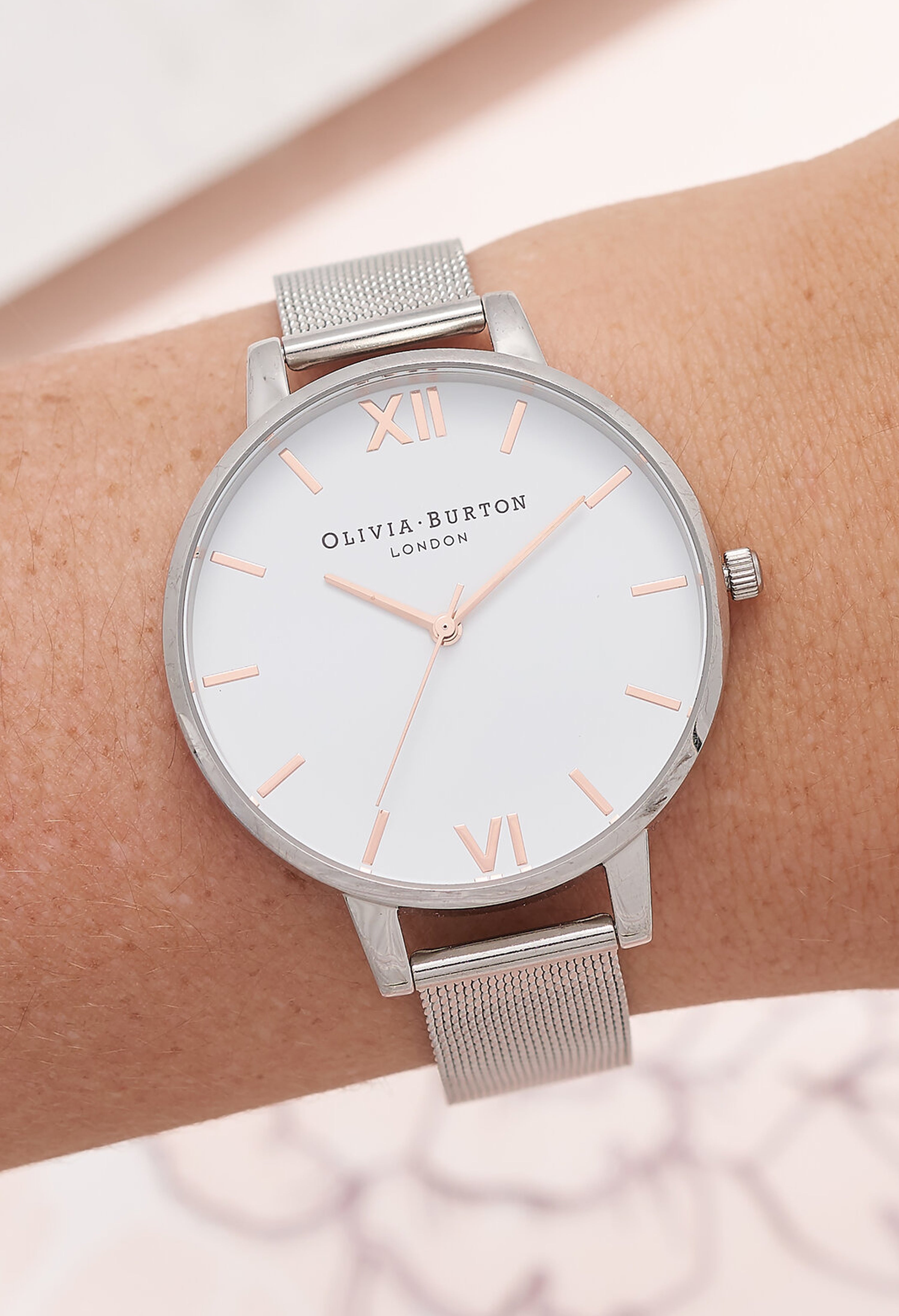 Wrist wearing an Olivia Burton stainless steel mesh watch with white dial; Ladies watch fashion close-up.