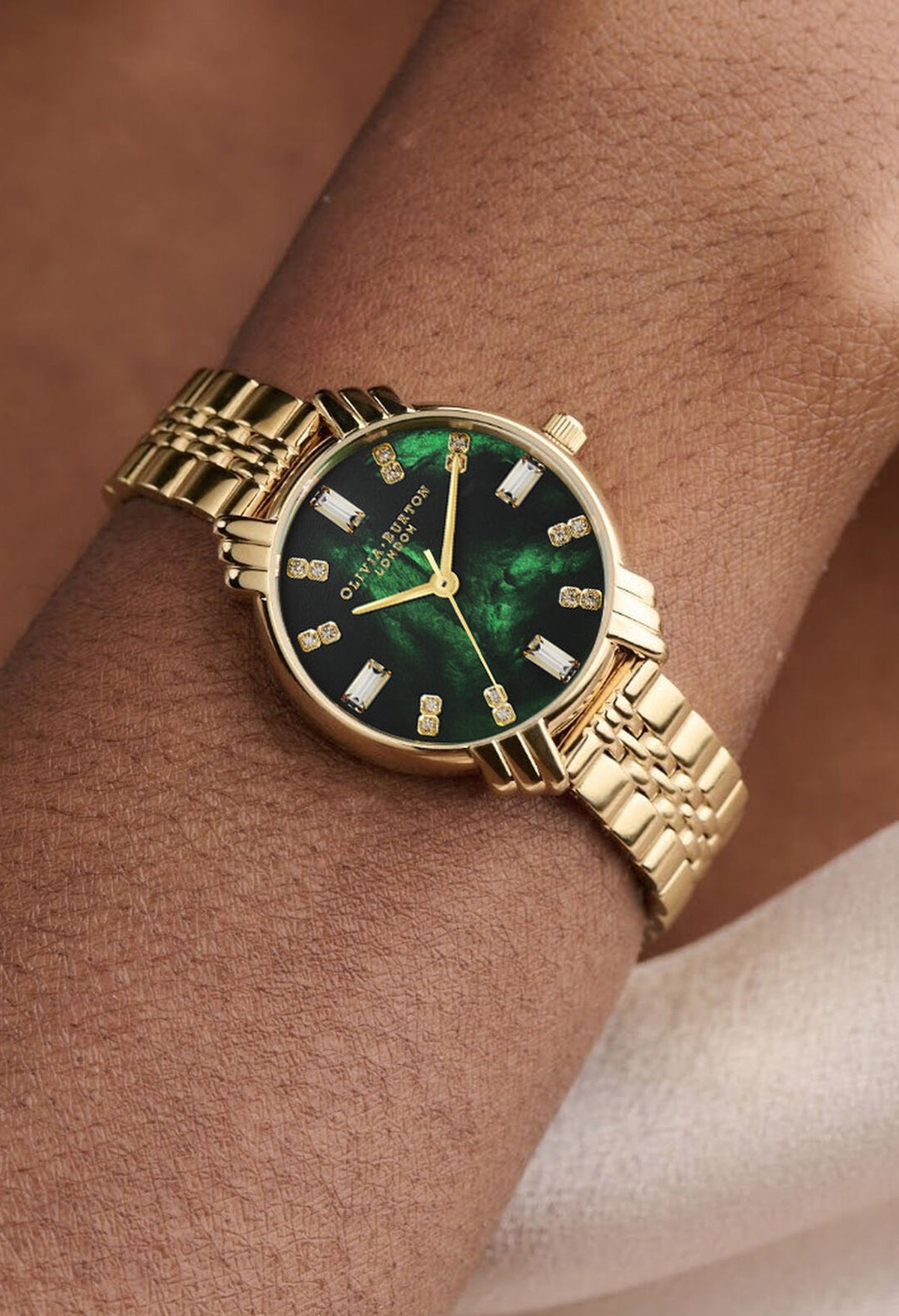 Close-up showcasing the Olivia Burton gold watch with a green Art Deco dial on a woman's wrist.