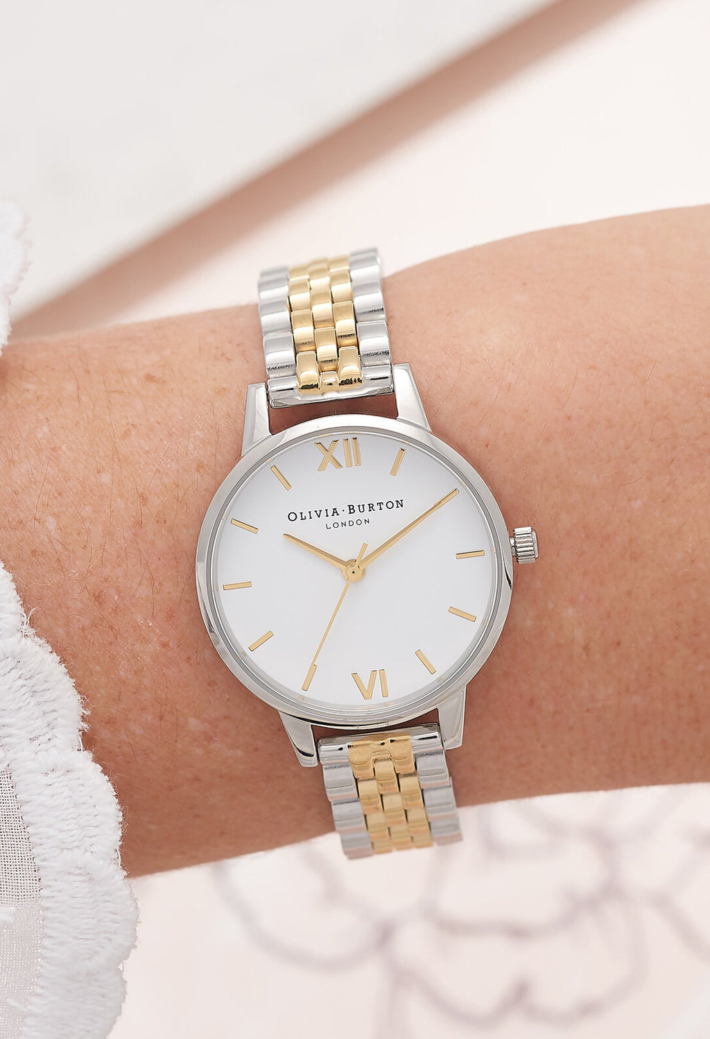 Olivia Burton watch on a woman's wrist. Classic white dial with a silver and gold bracelet band.