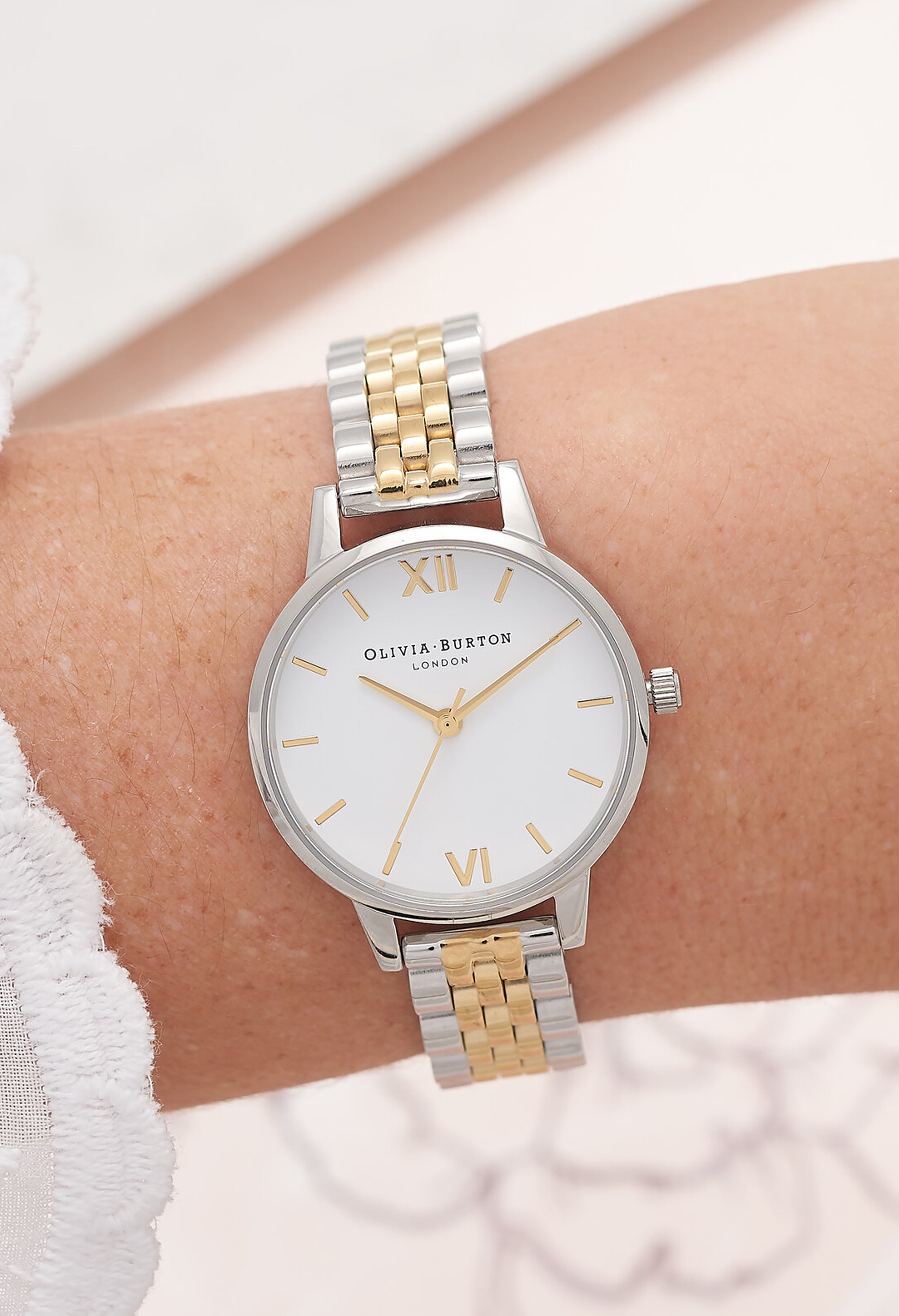 Olivia Burton watch on a woman's wrist. Classic white dial with a silver and gold bracelet band.