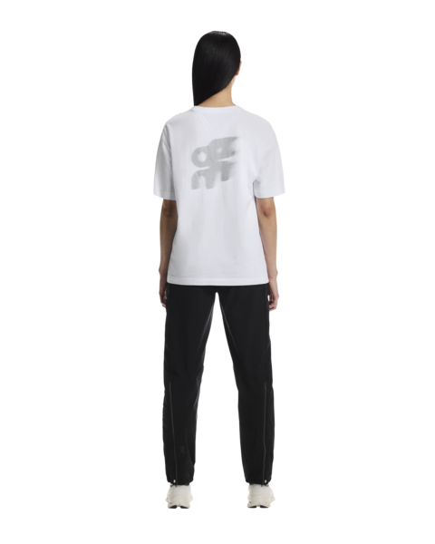 Person wearing a white t-shirt with a logo and black pants on a white background