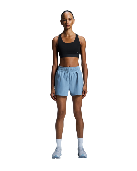 Woman wearing a black sports bra and light blue shorts on a white background