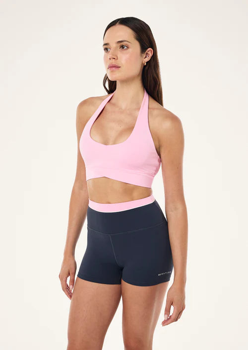 Woman wearing a pink sports bra and black shorts on a white background