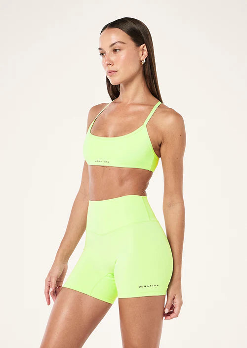 Woman wearing a neon green sports bra and shorts set on a white background