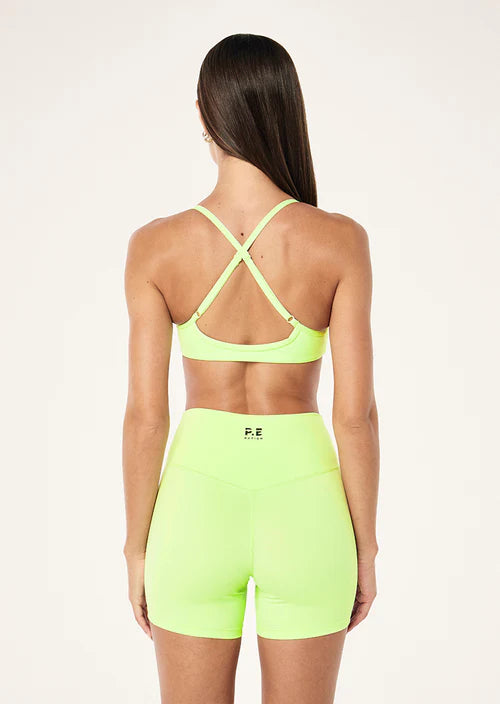 Woman wearing a neon green sports bra and shorts set on a white background