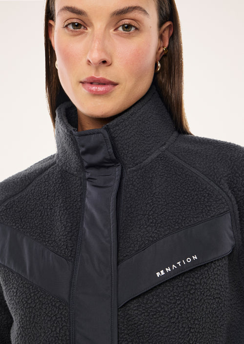 Woman wearing a dark blue fleece jacket with a visible brand logo on a light background