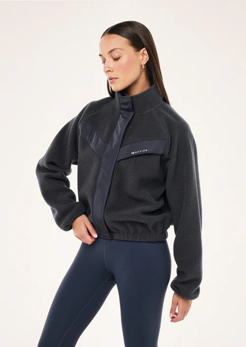 Woman wearing a dark blue fleece jacket with a brand logo on a white background