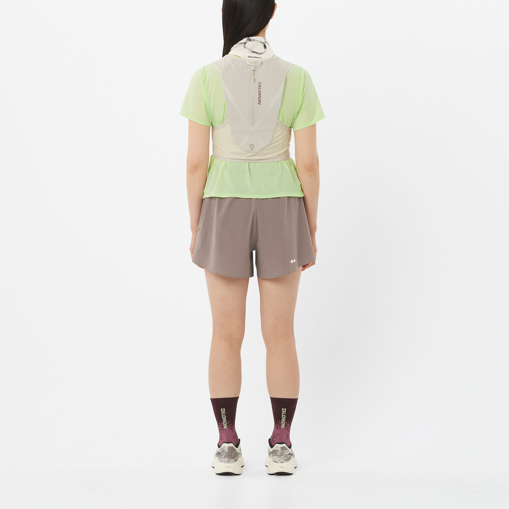 Person wearing a light green shirt, beige jacket, and gray shorts on a white background