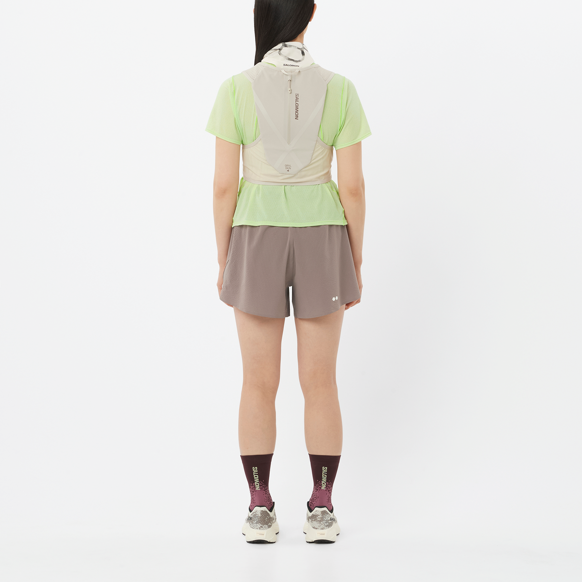 Person wearing a light green shirt, beige jacket, and gray shorts on a white background