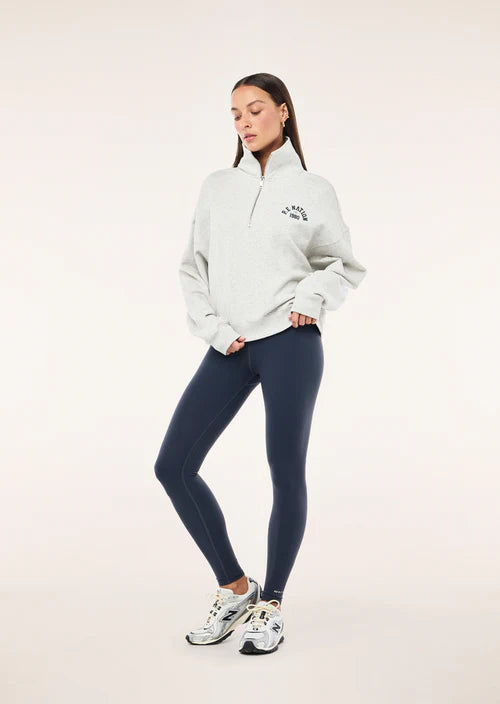 Woman wearing a white sweatshirt and dark blue leggings on a light pink background